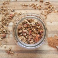 Top-down view of homemade pecan pie granola on a cutting board with a teaspoon of cinnamon and scattered granola.