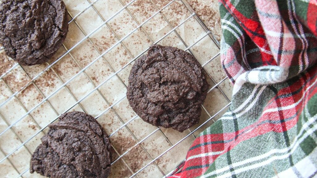 Freshly baked peppermint hot cocoa cookies cooling on a wire rack with a holiday plaid towel.