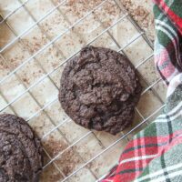 Freshly baked peppermint hot cocoa cookies cooling on a wire rack with a holiday plaid towel.