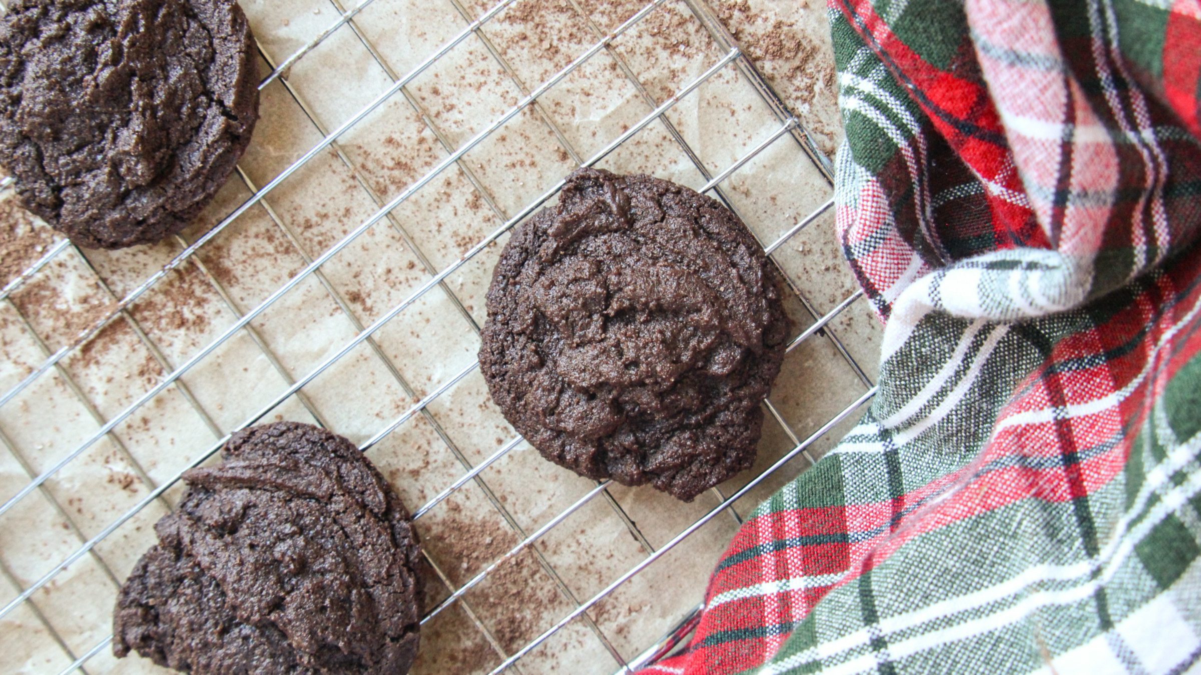 Freshly baked peppermint hot cocoa cookies cooling on a wire rack with a holiday plaid towel.