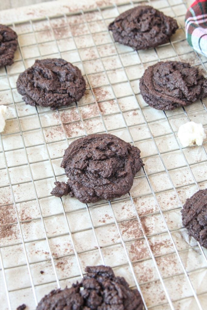 Fudgy peppermint hot cocoa cookies cooling on a wire rack, dusted with cocoa powder.