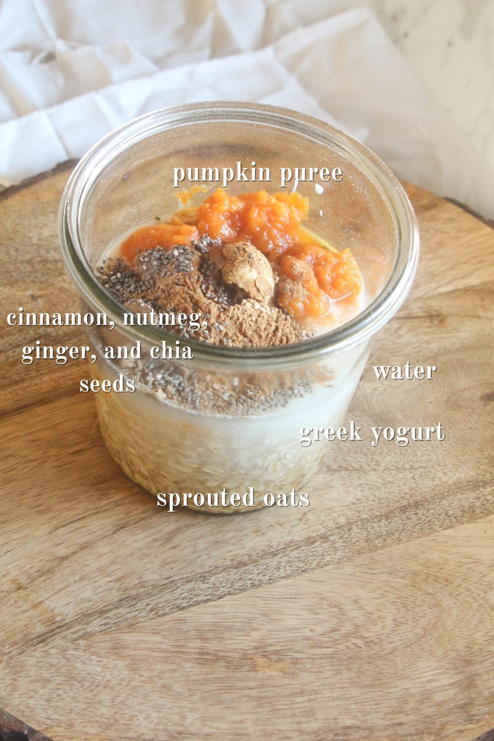Pumpkin overnight oats ingredients layered in a glass jar with pumpkin puree, oats, chia seeds, and spices