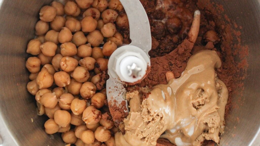 Unblended chocolate hummus ingredients in a food processor before blending into a smooth vegan dessert dip.