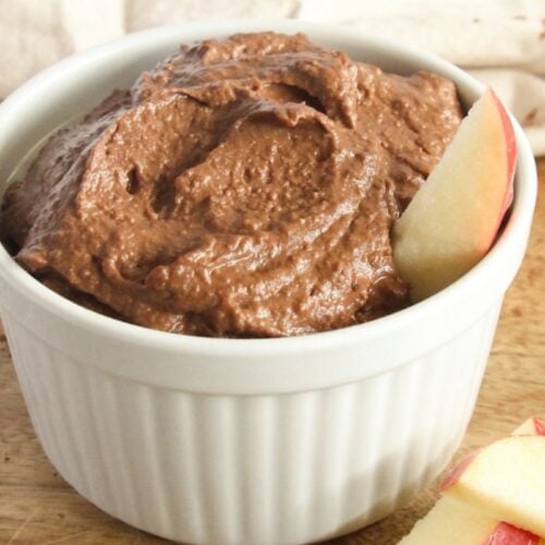 Creamy vegan chocolate hummus served in a bowl with fruit on the side
