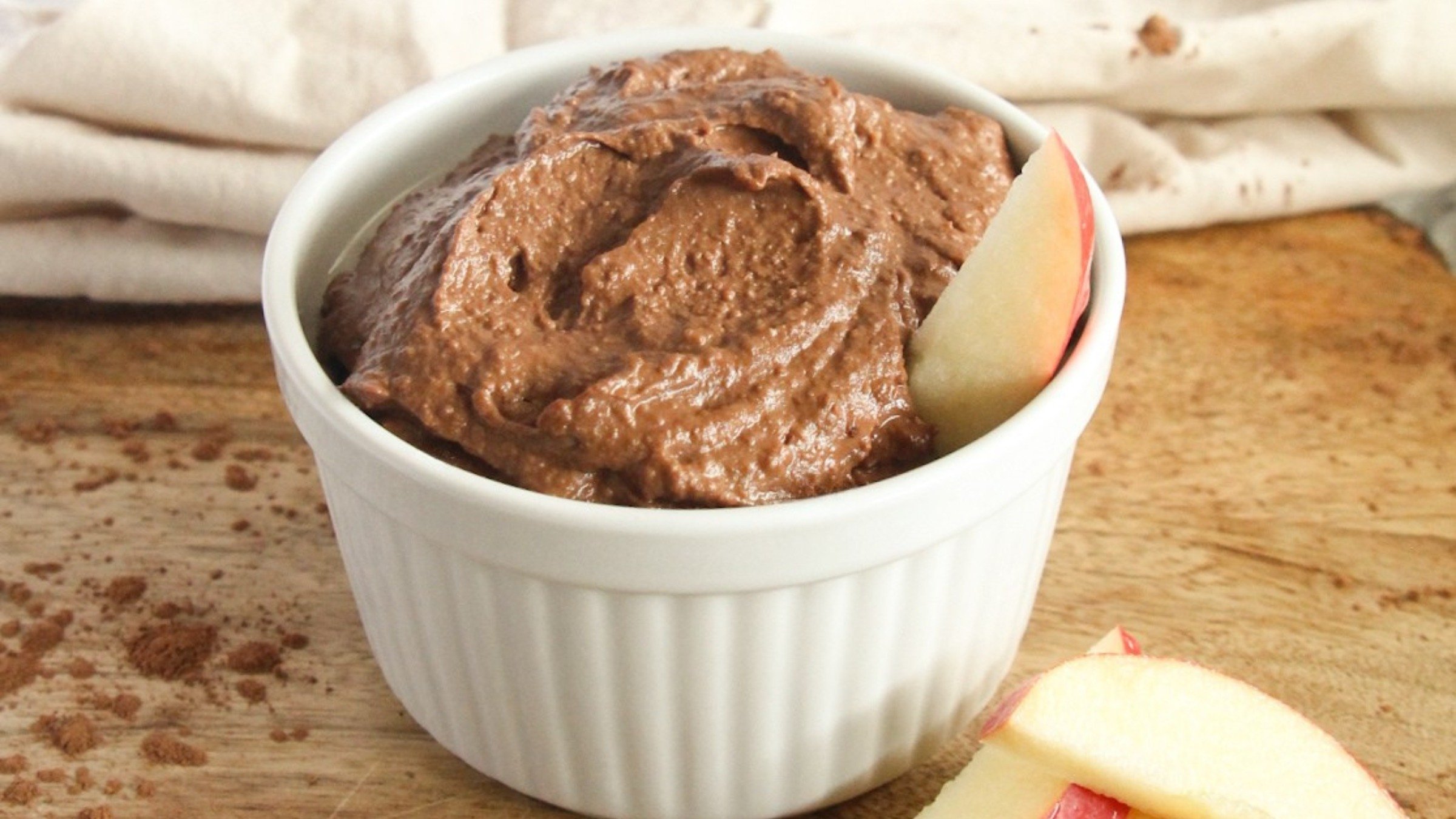 Creamy vegan chocolate hummus served in a bowl with fruit on the side