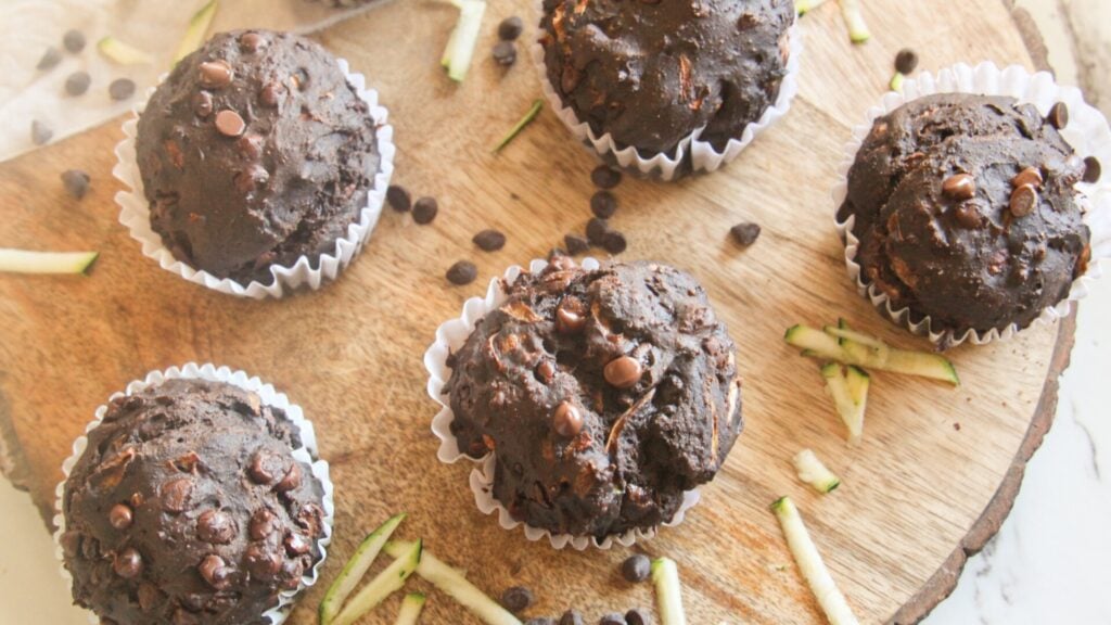 Chocolate zucchini muffins arranged on a wooden board with chocolate chips