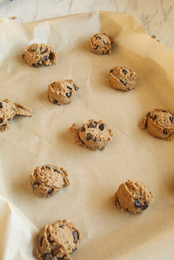 Raw chocolate chip cookie dough made with coconut sugar scooped into balls on a baking sheet.