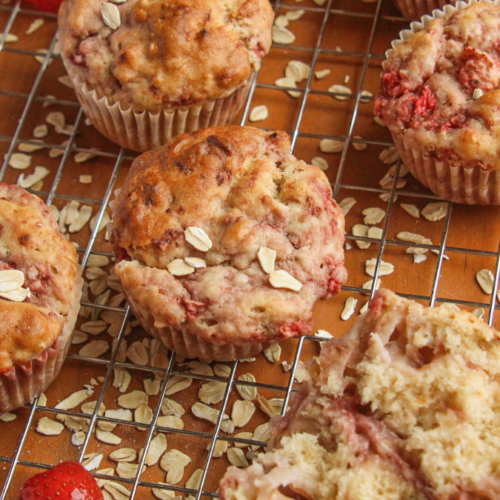 A collection of golden brown strawberry oatmeal muffins cooling on a wire rack, including one broken open to show the moist crumb.