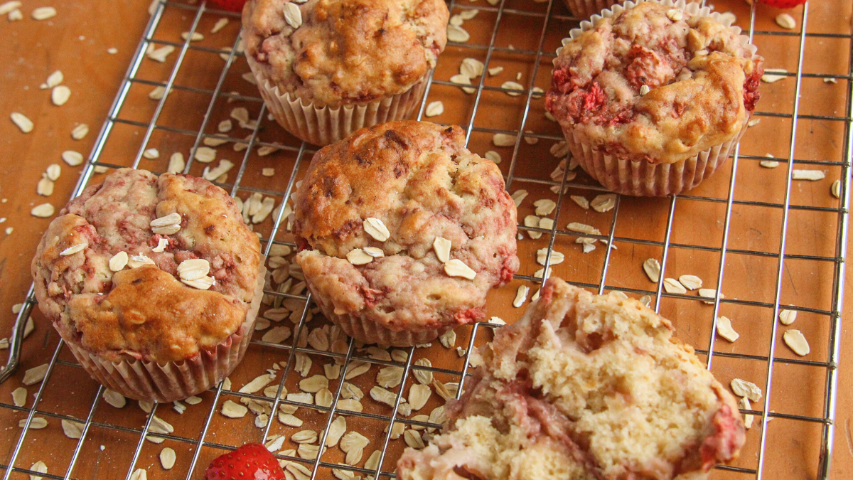 A collection of golden brown strawberry oatmeal muffins cooling on a wire rack, including one broken open to show the moist crumb.